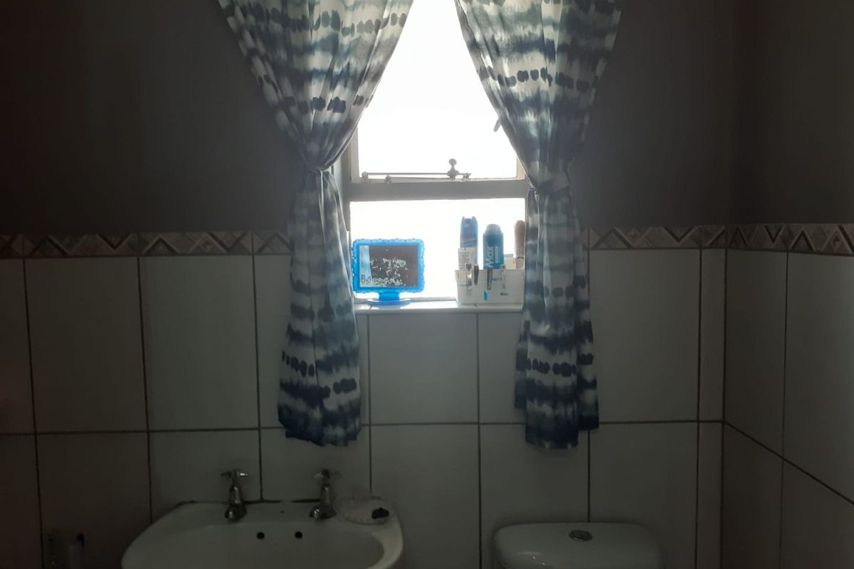 A functional bathroom featuring a pedestal basin, toilet, and classic white wall tiling with a decorative border.