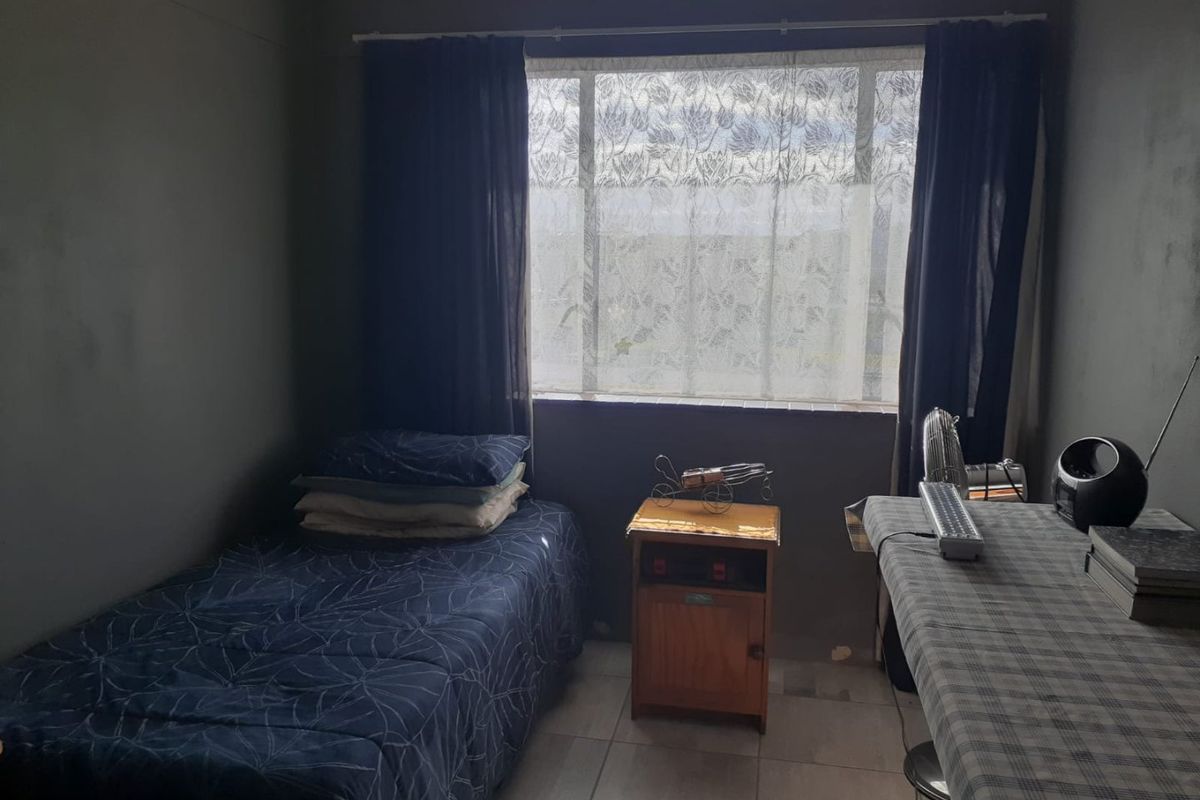 A compact bedroom featuring tiled flooring and a large window, currently finished with dark wall paint.