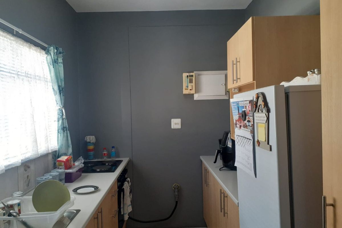 A functional galley-style kitchen featuring light wood cabinetry, laminate countertops, a built-in oven, and an electric hob.