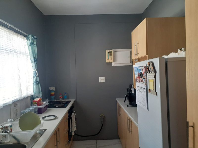 A functional galley-style kitchen featuring light wood cabinetry, laminate countertops, a built-in oven, and an electric hob.