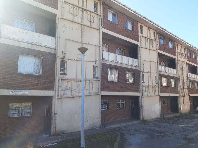 Exterior view of a multi-story apartment building featuring brick facade, external plumbing, and balconies with security gates.