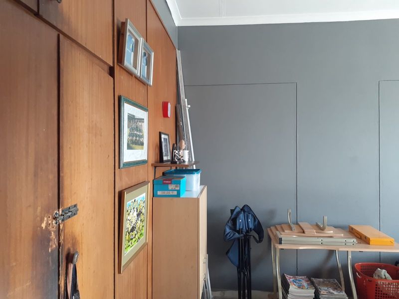 A bedroom interior featuring floor-to-ceiling wooden built-in cupboards with visible wear and a contrasting grey accent wall.
