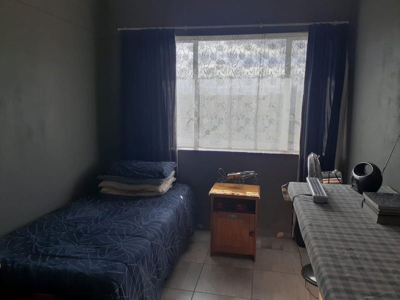 A compact bedroom featuring tiled flooring and a large window, currently finished with dark wall paint.