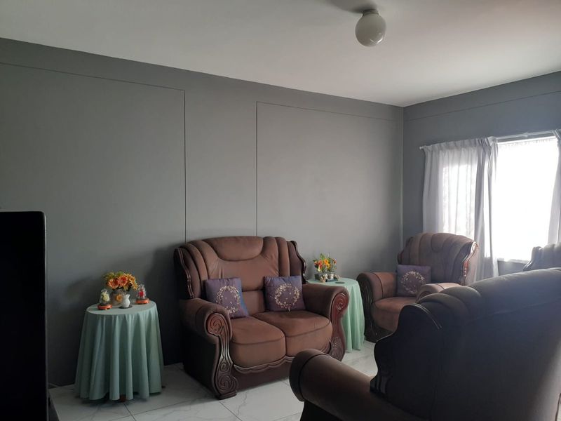 A living room featuring grey painted walls, tiled flooring, and natural light from a window with curtain tracks.