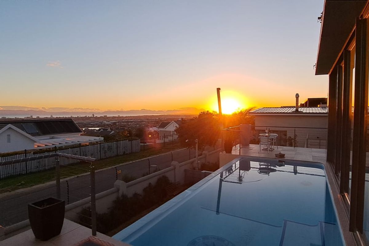 An elevated outdoor pool area featuring a modern glass balustrade and expansive sunset views over the surrounding neighborhood.