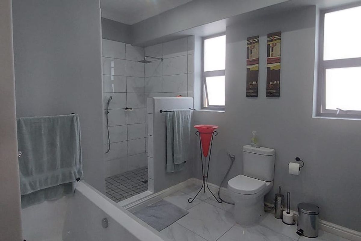 Modern bathroom featuring a walk-in shower, bathtub, and vanity with neutral grey walls and tiled flooring.