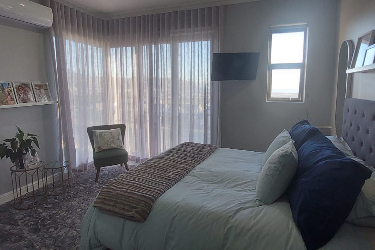 A well-maintained bedroom featuring a split-system air conditioner, large sliding glass doors with sheer curtains, and neutral wall finishes.