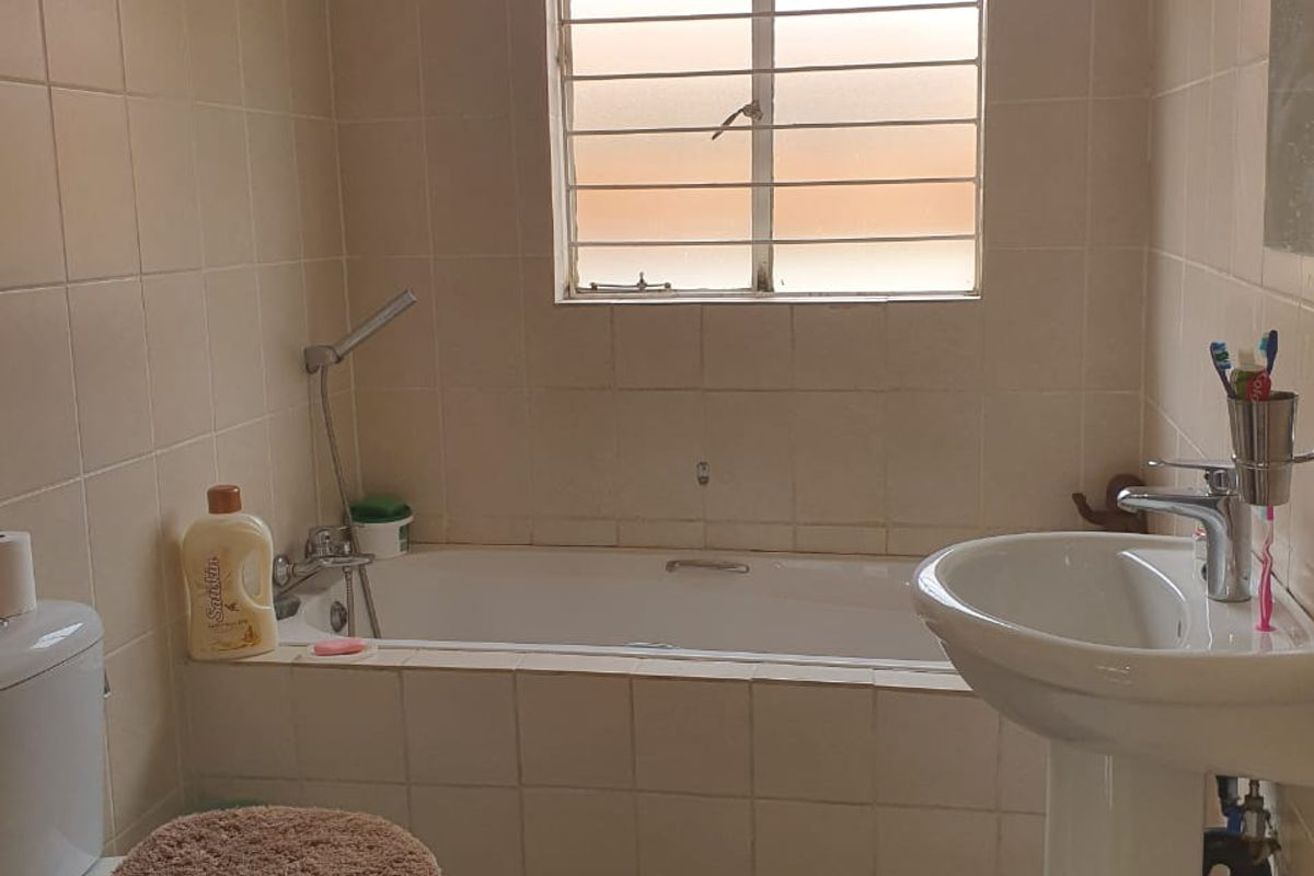 A dated bathroom featuring a bathtub, pedestal basin, and toilet with neutral wall and floor tiling.