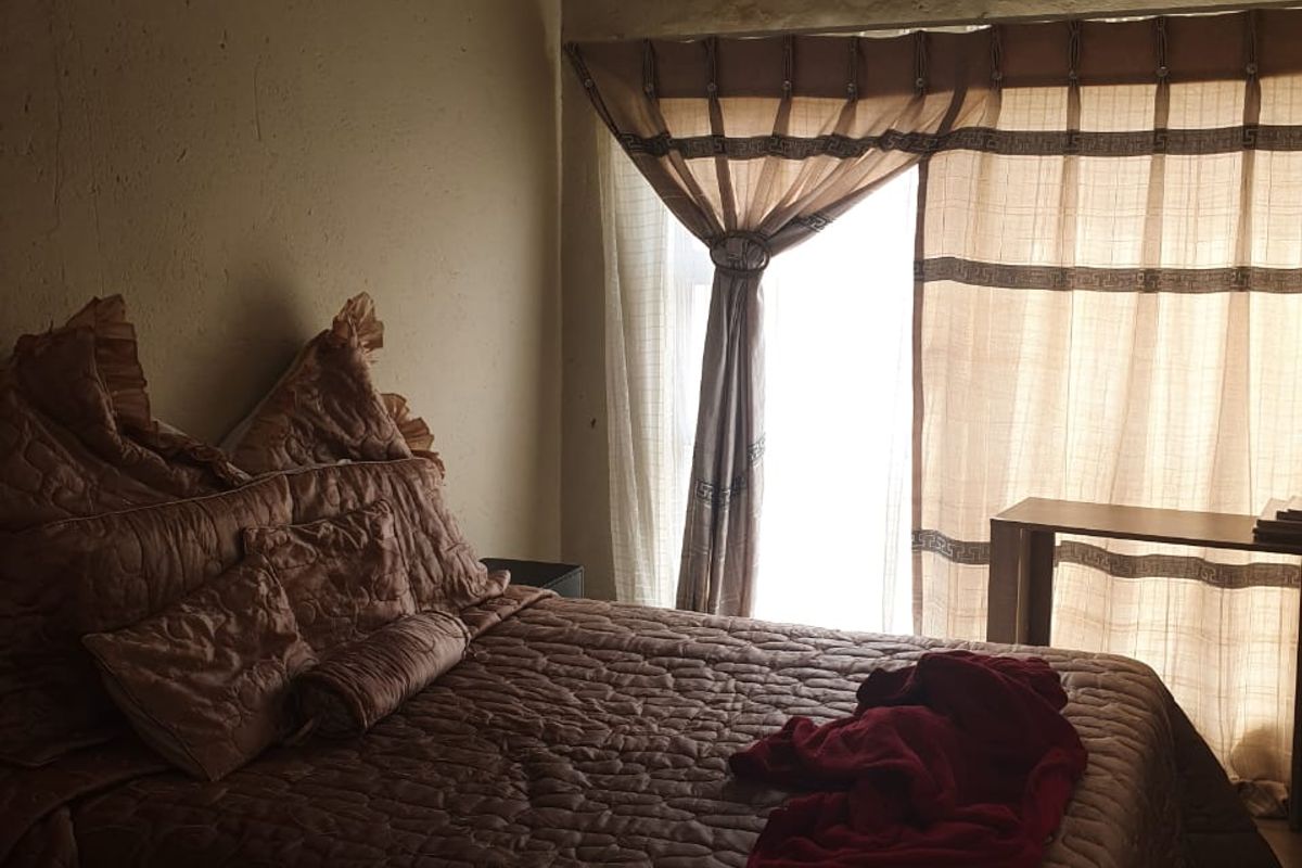 A bedroom featuring tiled flooring and a sliding glass door providing natural light. The walls show signs of wear and require cosmetic attention.