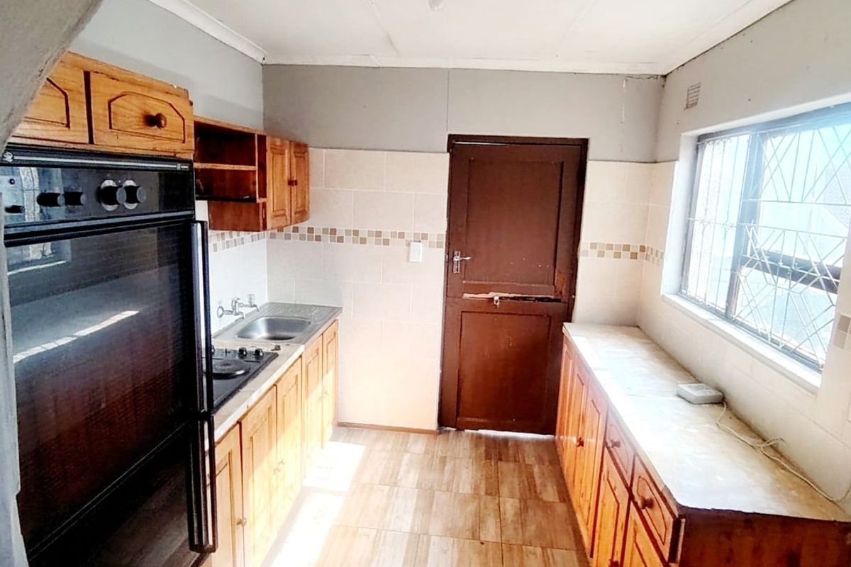 A functional kitchen featuring built-in wooden cabinetry, integrated oven, hob, and tiled flooring, offering a blank canvas for potential modern updates.