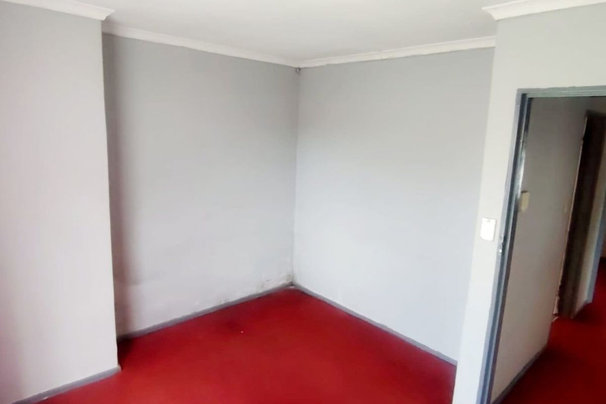 An empty bedroom featuring red flooring and neutral grey walls, providing a blank canvas for renovation or interior design updates.