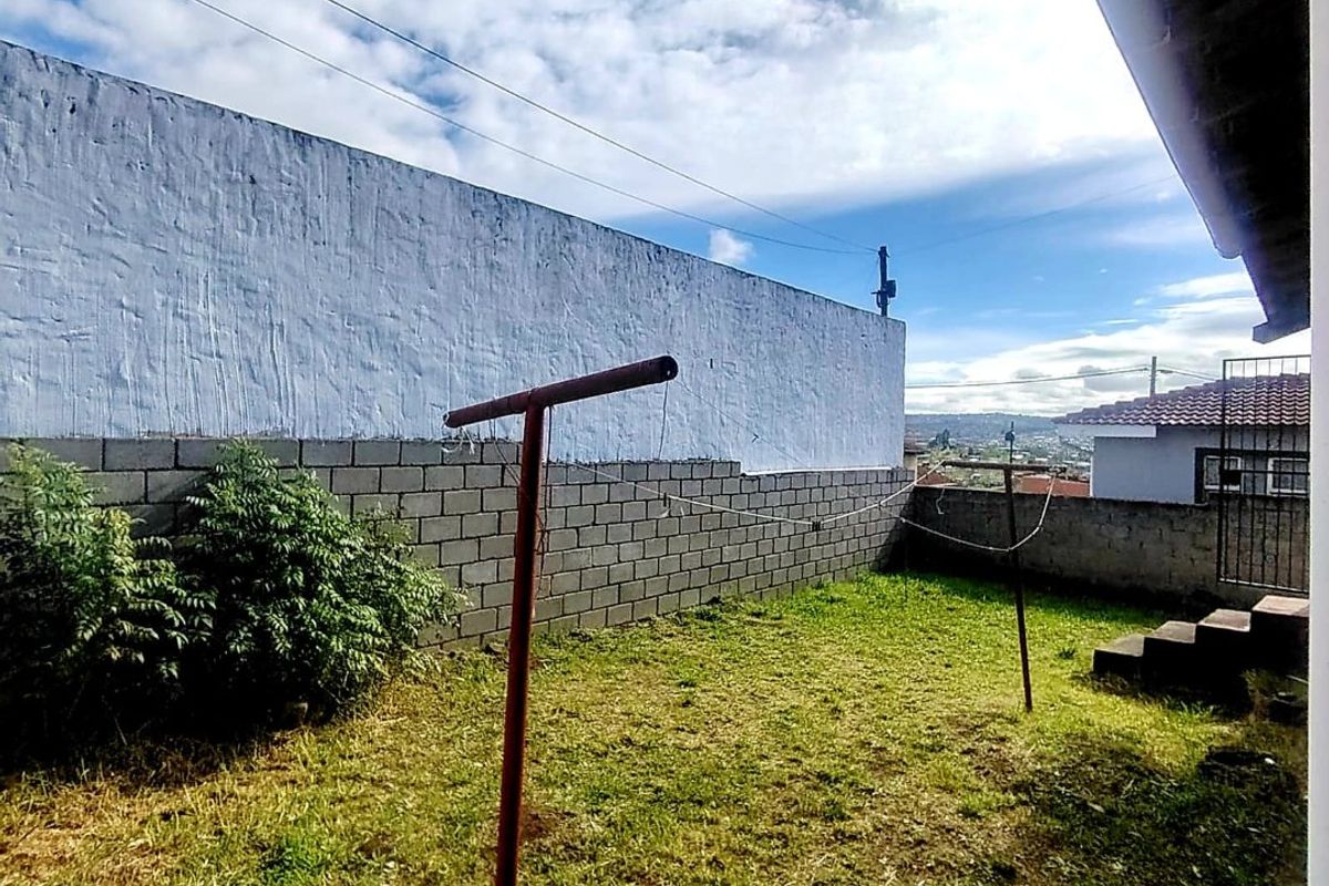 A rear garden area featuring a concrete block boundary wall, lawn space, and concrete steps leading to the property.