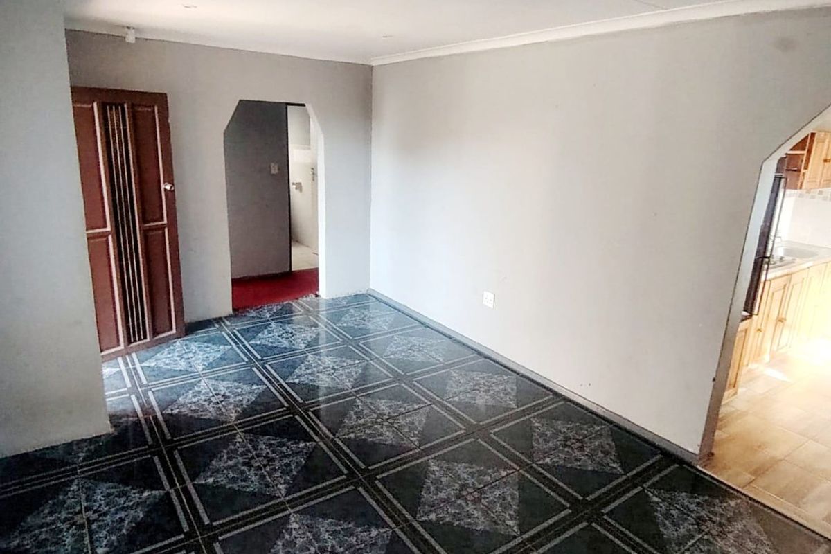 An empty living area featuring patterned tiled flooring and an arched entryway leading to the kitchen and adjacent rooms.