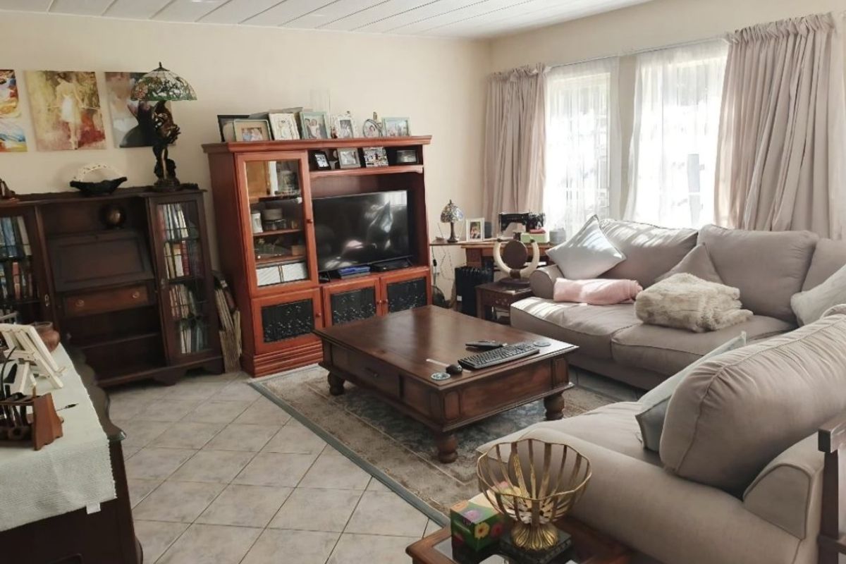 A comfortable living room featuring tiled flooring, a panelled ceiling, and large windows with curtains, providing a bright and functional space.