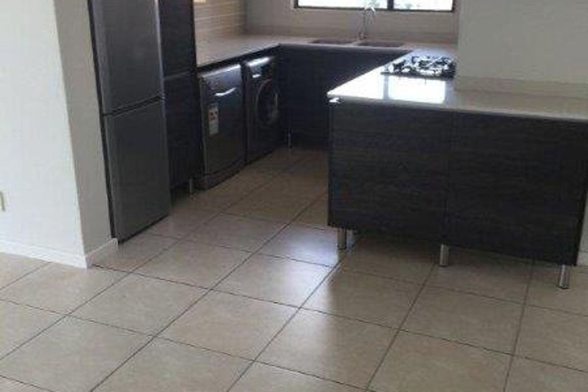 Modern kitchen featuring dark cabinetry, stone countertops, gas hob, extractor fan, and tiled flooring in an open-plan layout.