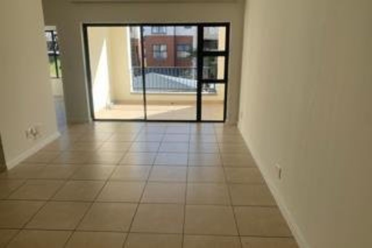 A bright, empty living area featuring neutral tiled flooring and large sliding glass doors that open onto an outdoor balcony space.
