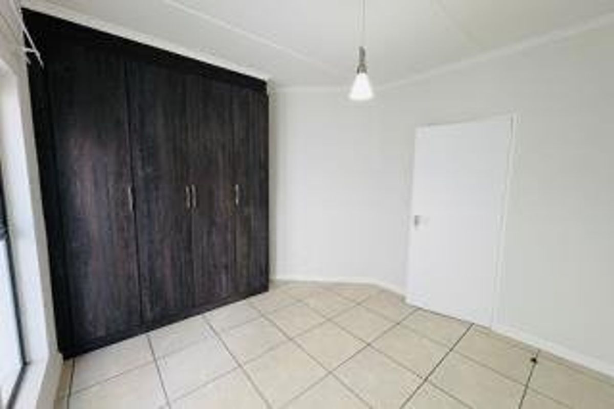 A clean, empty bedroom featuring dark wood-finish built-in cupboards, neutral tiled flooring, and a simple pendant light fixture.