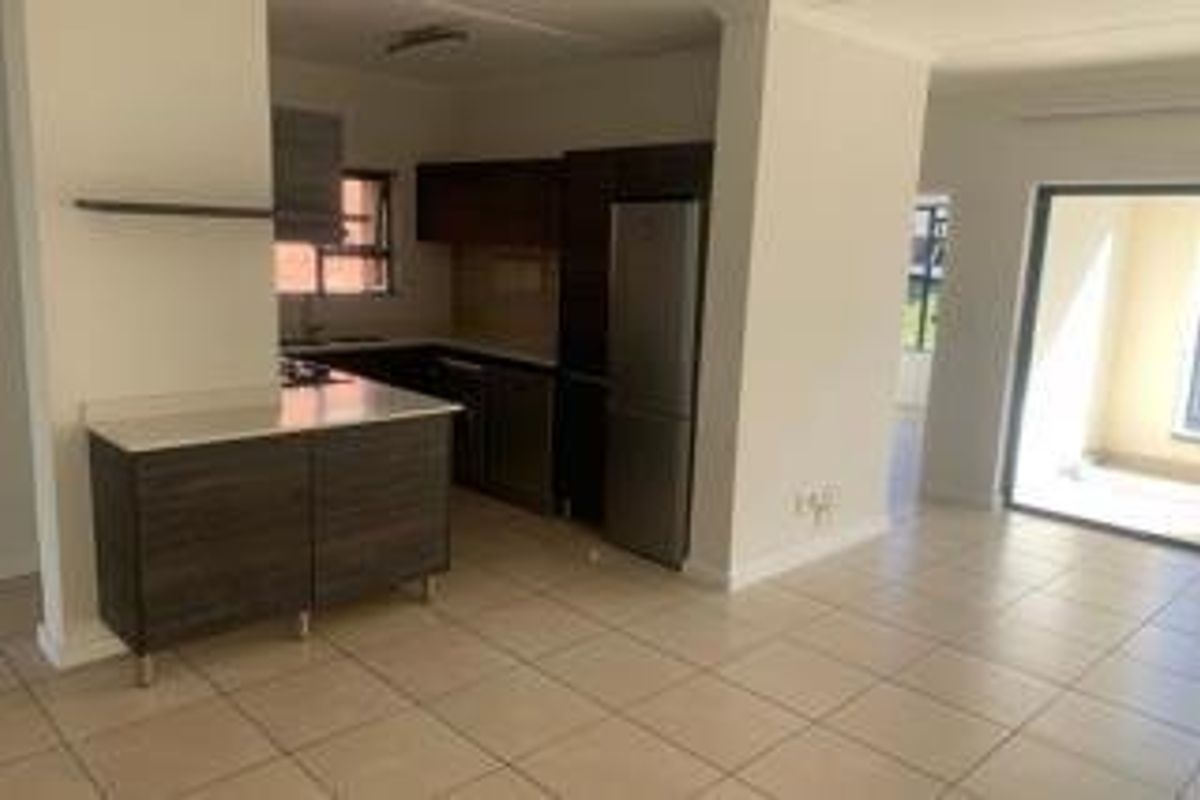 Open-plan kitchen and living area featuring modern dark cabinetry, stone countertops, tiled flooring, and direct access to an outdoor patio through sliding glass doors.