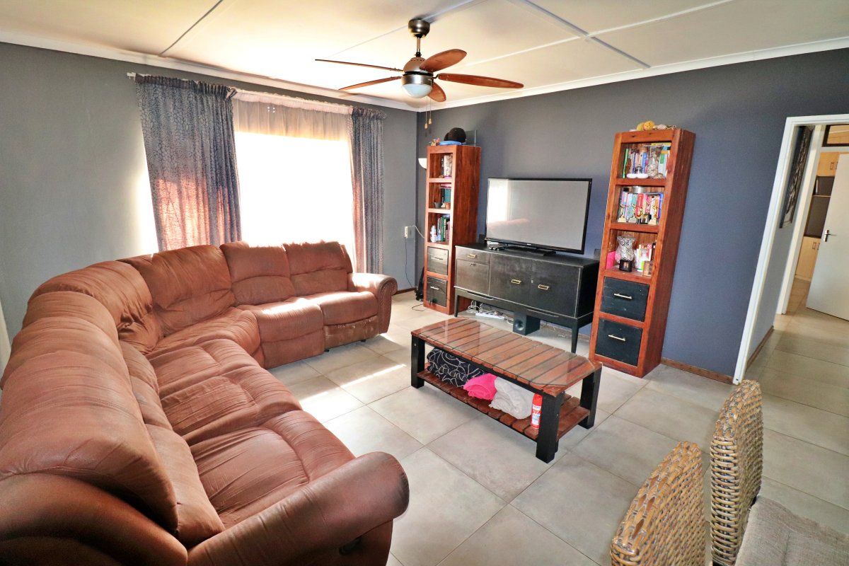 A living room featuring tiled flooring and a ceiling fan, with dark grey walls and visible ceiling panel joints.