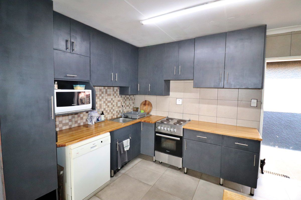 A functional kitchen featuring dark grey cabinetry, wooden countertops, tiled backsplash, and integrated appliances including a built-in microwave and freestanding oven.