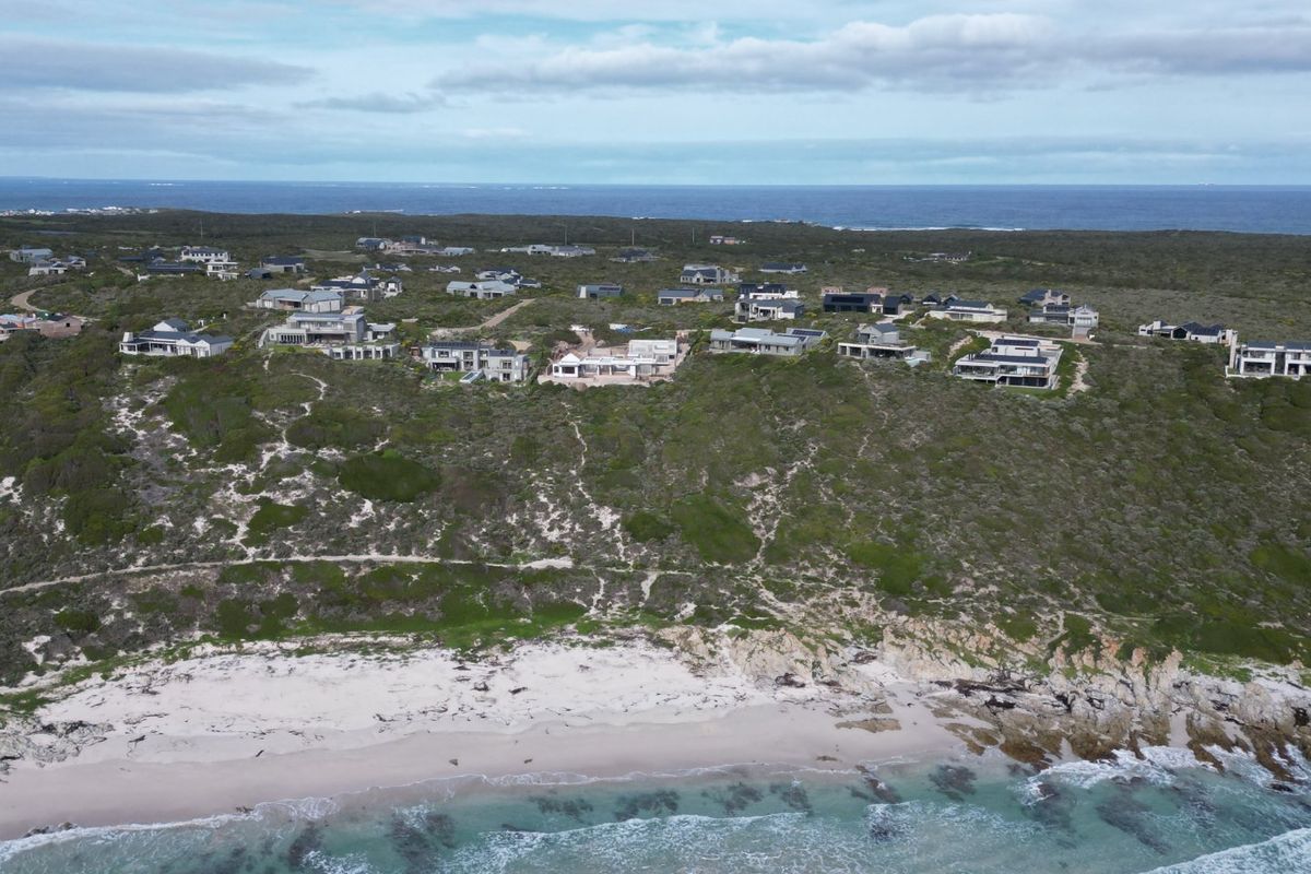 An aerial view of a coastal residential estate situated on a hill overlooking the ocean and sandy beach.