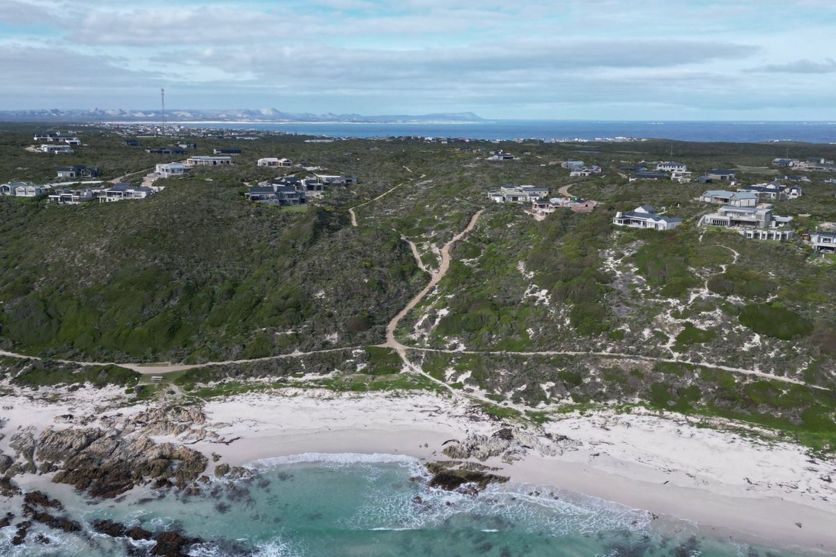 An aerial view of a coastal residential area featuring natural vegetation, sandy beaches, and rocky shorelines with established homes in the background.