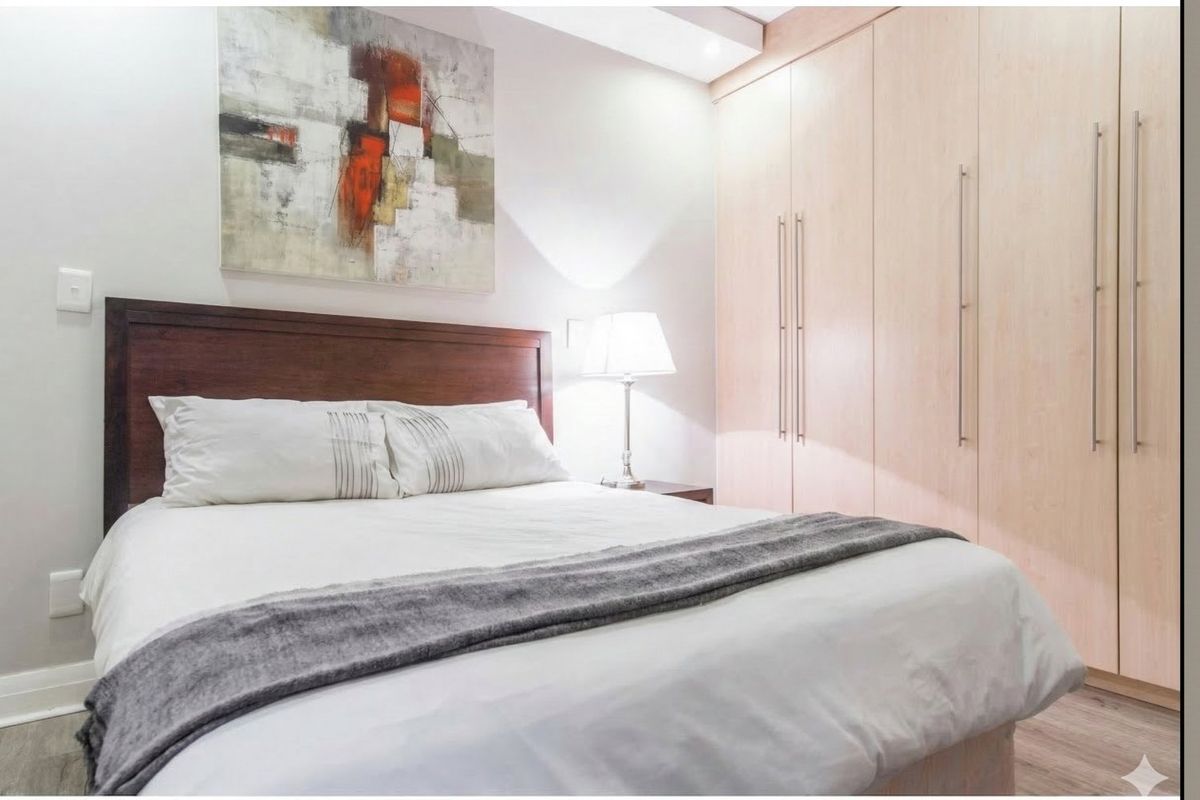 A well-maintained bedroom featuring light wood-toned built-in cupboards, laminate flooring, and recessed ceiling lighting.