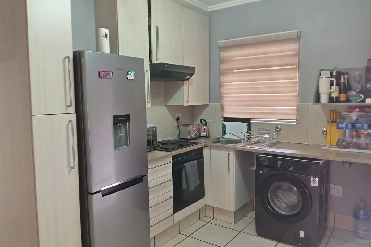 Functional kitchen featuring light wood-finish cabinetry, tiled flooring, integrated oven and hob, and space for a washing machine.