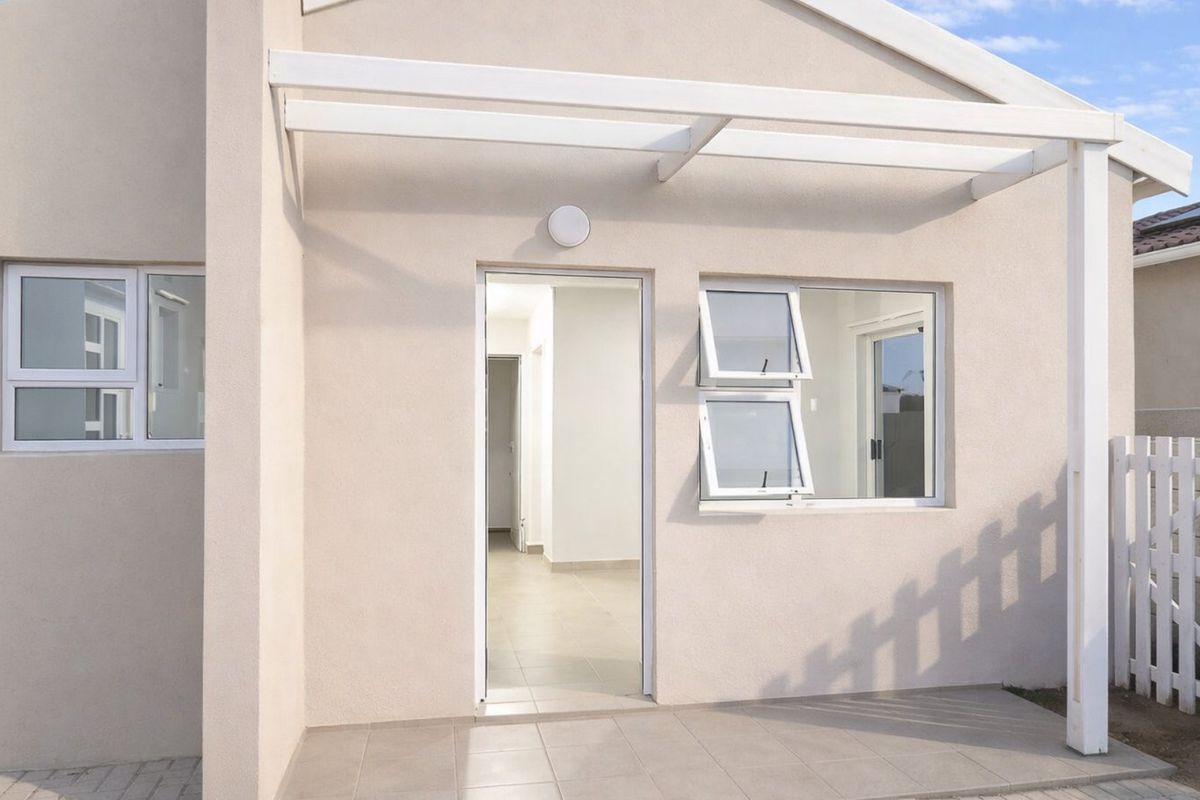 A neat rear exterior view of a townhouse featuring a tiled patio, pergola, and white picket fencing.