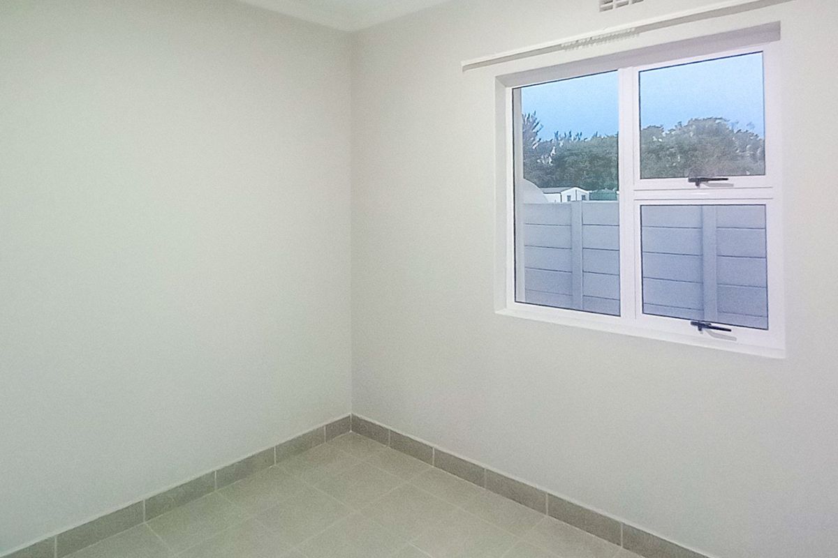 A clean, empty bedroom featuring neutral tiled flooring and a modern aluminium window frame, providing a bright and versatile space.