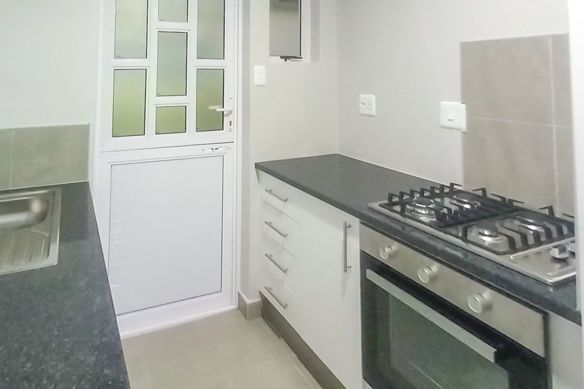 A clean, functional kitchen featuring built-in cabinetry, a gas hob, an integrated oven, and a stainless steel sink with direct exterior access.