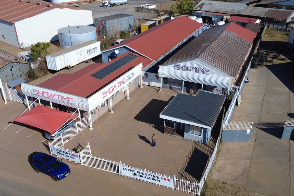 Aerial view of an industrial property featuring multiple warehouse buildings, paved yard space, perimeter fencing, and solar panel installations.