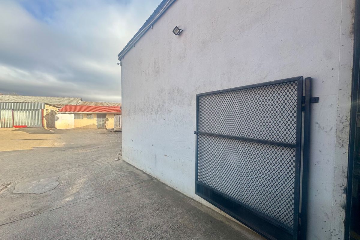 Rear exterior view of an industrial property featuring a security gate, concrete paving, and exterior wall lighting.