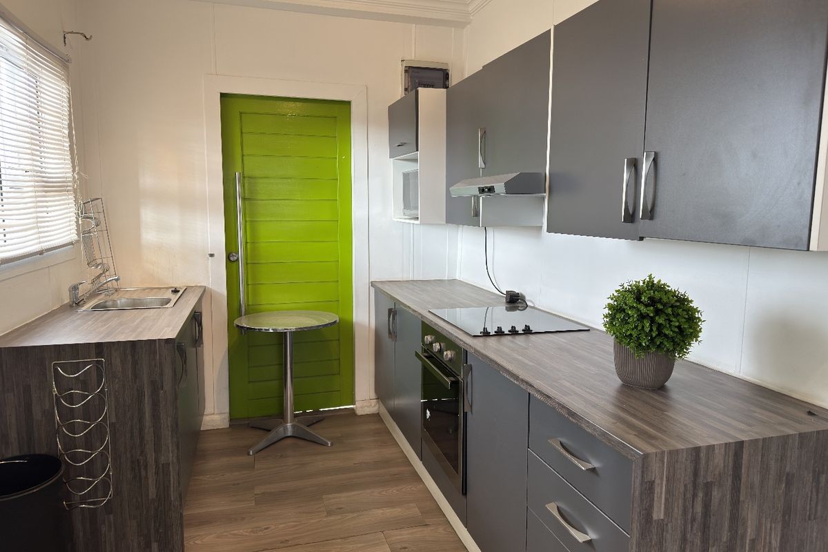 A compact, modern kitchen featuring grey cabinetry, laminate countertops, an integrated oven with cooktop, and a stainless steel sink.