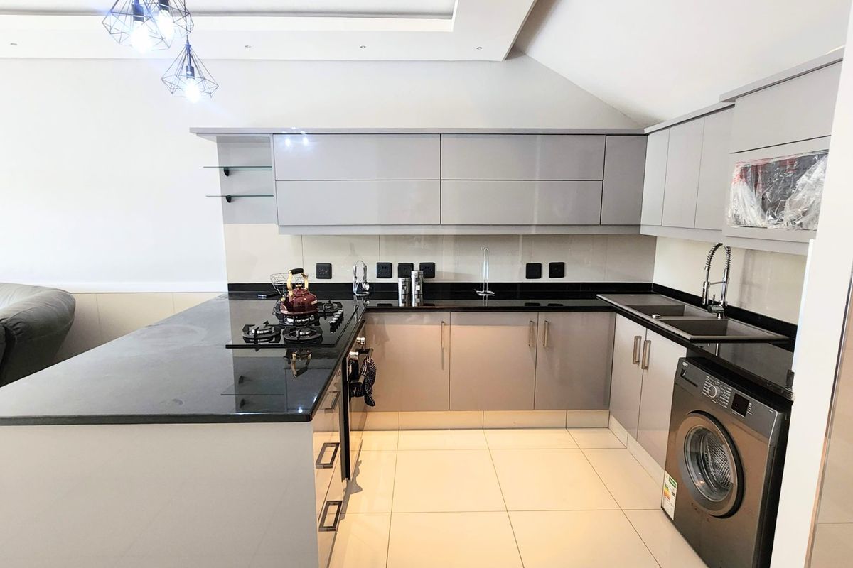 Modern kitchen featuring sleek grey cabinetry, black granite countertops, gas hob, and integrated sink, complemented by contemporary pendant lighting and tiled flooring.
