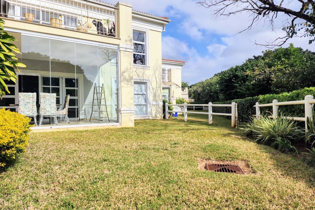 Rear view of the apartment featuring a glass-enclosed patio, an upper-level balcony with metal railings, and a private lawn area with perimeter fencing.