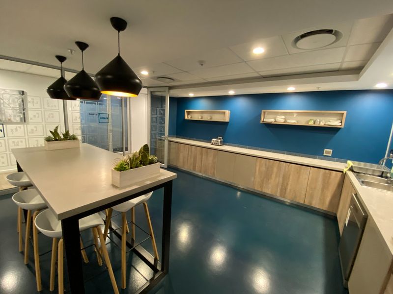 Modern commercial kitchen featuring sleek wood-finish cabinetry, stone countertops, blue accent walls, and a central island with pendant lighting.