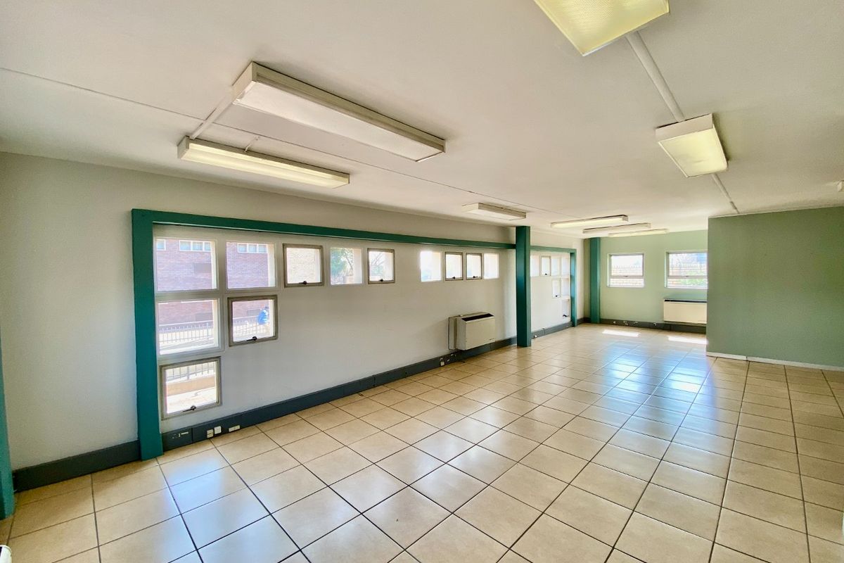 A spacious, empty commercial office area featuring ceramic tiled flooring, multiple casement windows, and integrated fluorescent lighting.