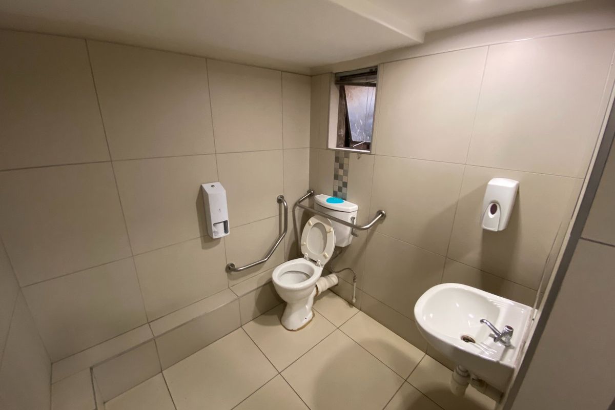 A functional commercial bathroom featuring tiled surfaces, a wall-mounted basin, and accessibility grab rails.