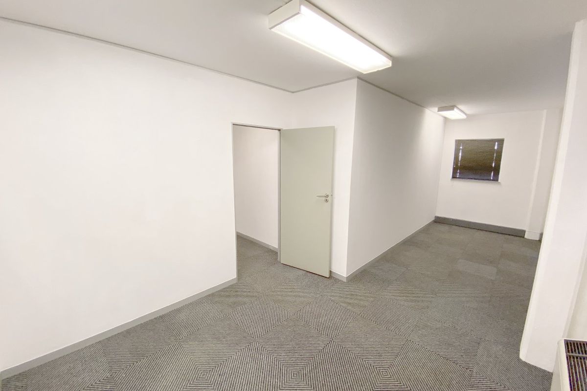 A clean, vacant office space featuring neutral walls, patterned carpet tiles, and functional overhead fluorescent lighting.