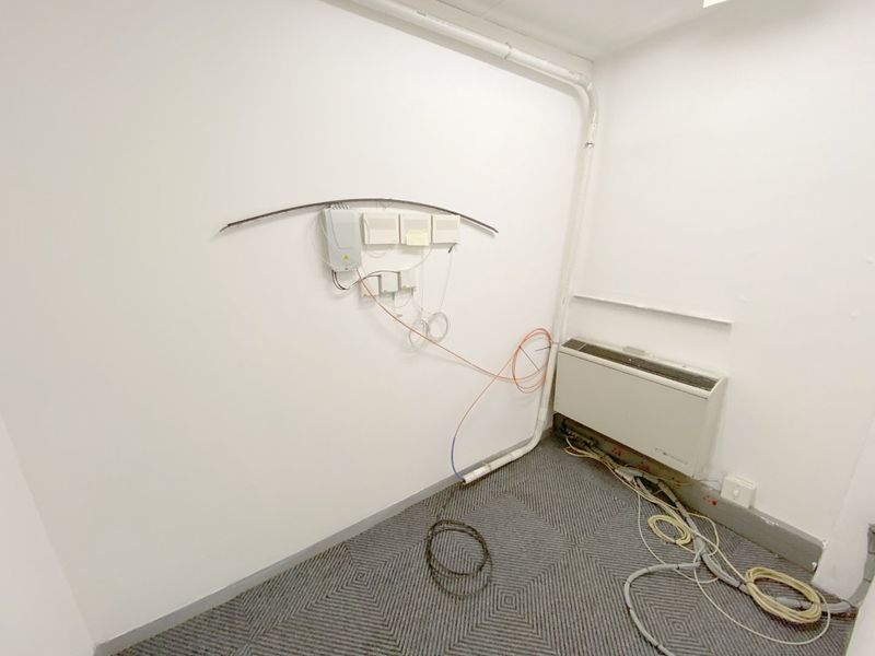 A utility space featuring exposed electrical and fiber optic infrastructure, wall-mounted HVAC unit, and carpeted flooring.