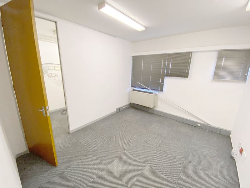 A vacant commercial office space featuring carpet tiles, fluorescent lighting, venetian blinds, and an integrated HVAC unit.