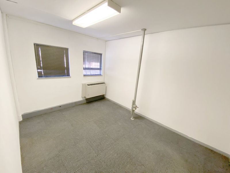 A vacant commercial office space featuring carpeted flooring, an integrated HVAC unit, and functional window blinds.
