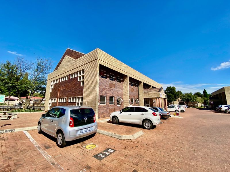 A commercial office building featuring a classic brick facade, pitched roof design, and an adjacent paved parking area for tenants and visitors.