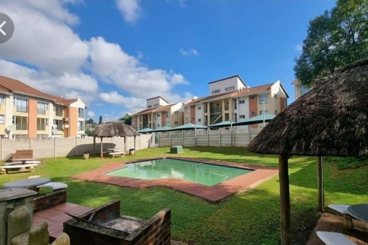 Communal outdoor area featuring a swimming pool, brick braai facilities, and thatched lapas within a secure apartment complex setting.