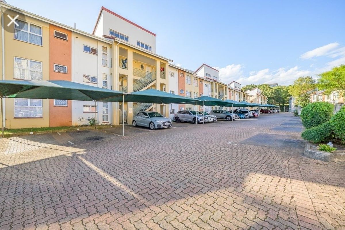 Exterior view of an apartment complex featuring a paved parking area with shade cloth carports and accessible stairwells.