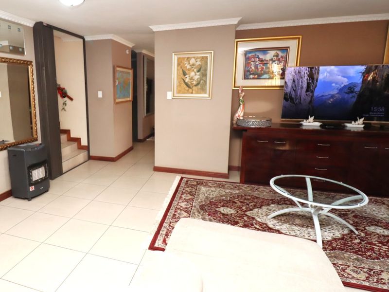 A spacious living room featuring tiled flooring, crown molding, and direct access to an internal staircase.