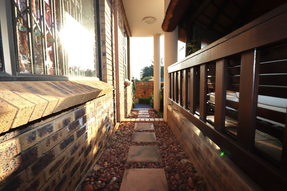 A narrow side walkway featuring a brick facade, stone stepping stones, pebble ground cover, and a timber railing leading to a rear outdoor area.