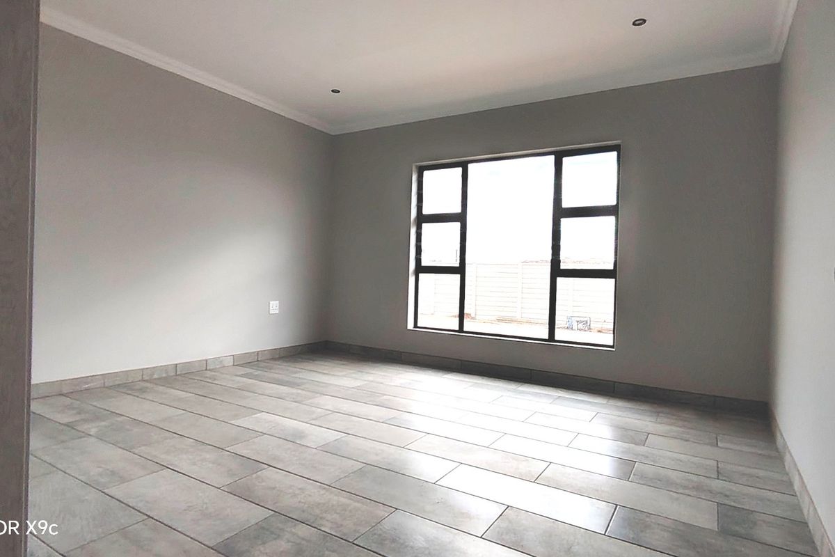 A bright, empty bedroom featuring modern grey tiled flooring, recessed downlighting, and large aluminium-framed windows, offering a clean and neutral blank canvas.