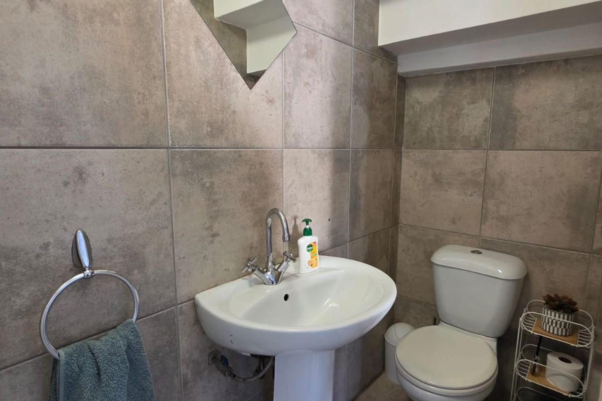 A compact bathroom featuring a pedestal basin with chrome mixer tap, toilet, and neutral ceramic wall tiling.